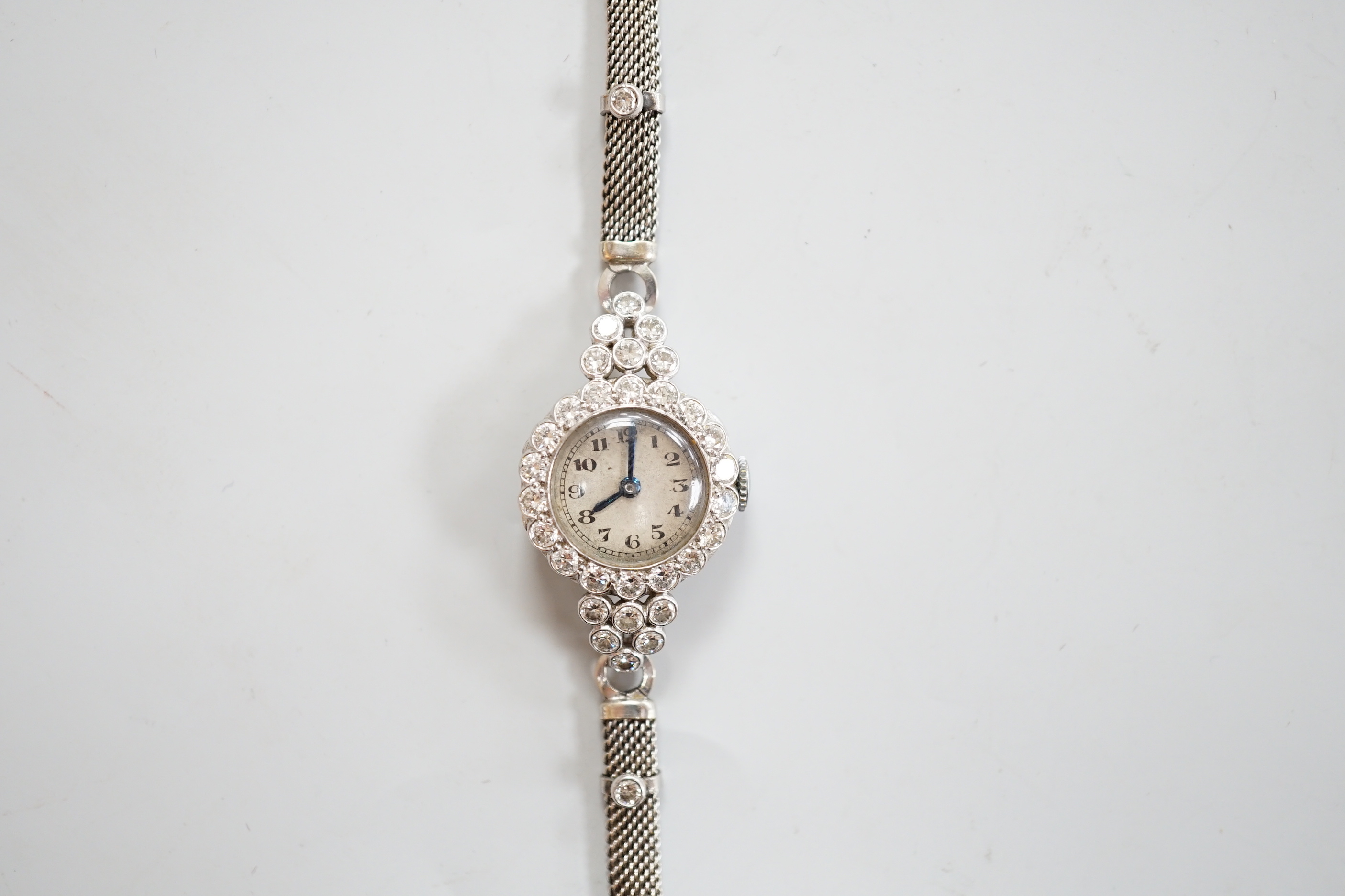 A lady's white metal and diamond set Movado manual wind cocktail watch, on a diamond set 9ct white metal mesh link bracelet, gross weight 18 grams.